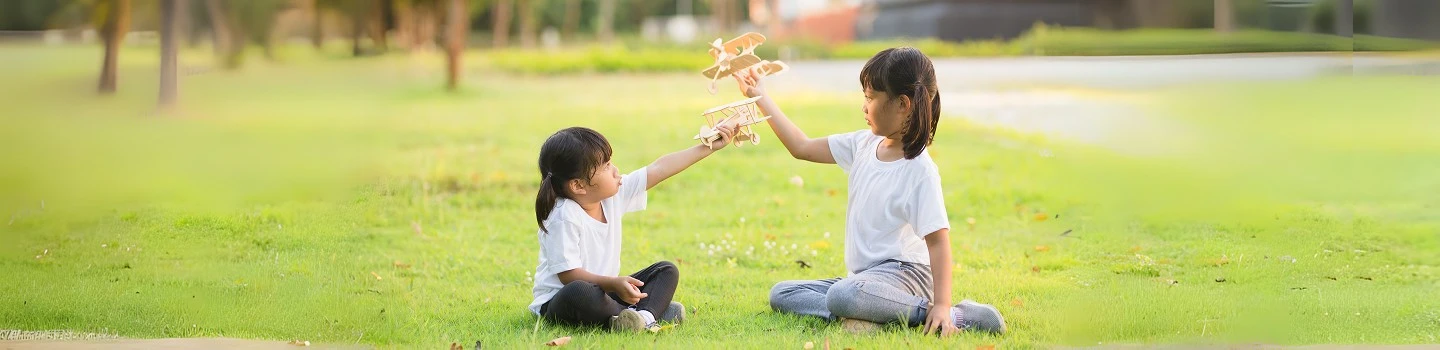 Two children playing with paperplane in grass field 