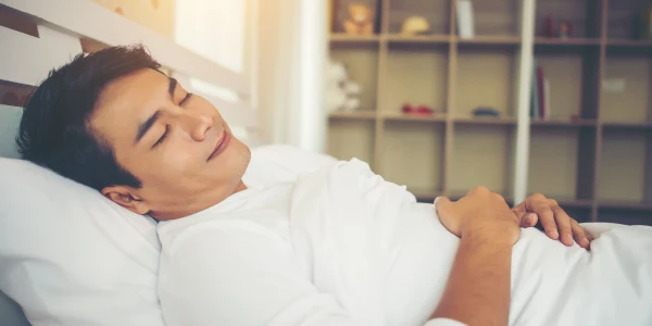 A man resting peacefully on a bed with a serene expression, representing deep sleep and relaxation.