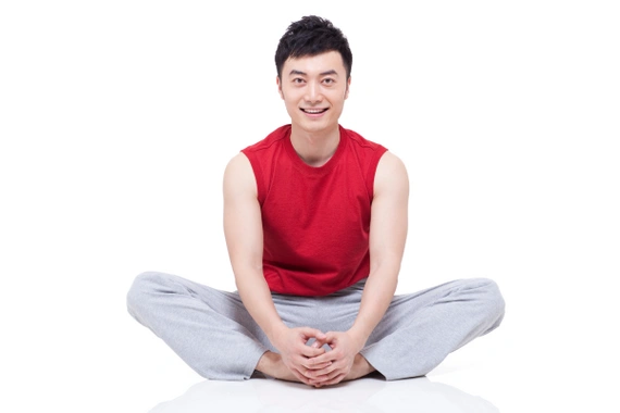 A smiling woman sitting cross-legged on the grass, practicing meditation on a sunny day